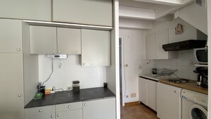 Een kleine keuken met witte kasten, een magnetron, een fornuis en een wasmachine.