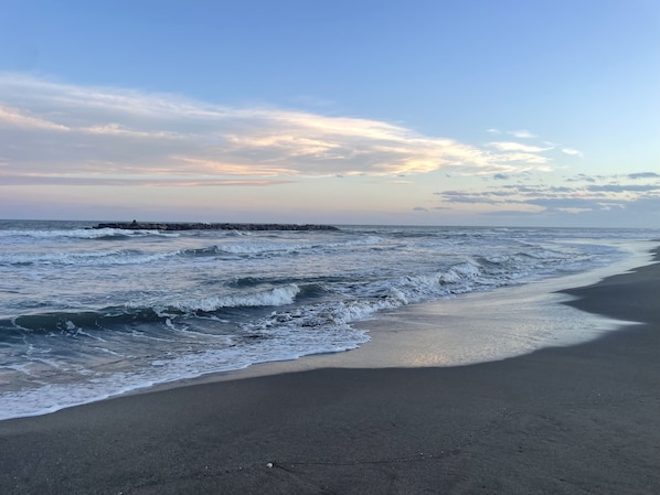 A beach with waves and a rocky breakwater in the distance.