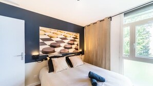 A modern bedroom with a large bed, a headboard with a geometric pattern, and a view of greenery through a window.