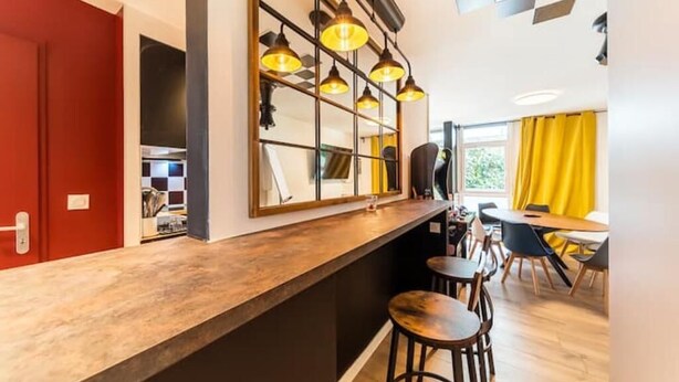 A modern kitchen with a wooden countertop, pendant lights, and a dining area with chairs and a table.