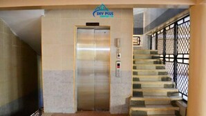 Un ascenseur sur lequel est apposée une pancarte, un escalier doté de rampes en métal et un sol carrelé.