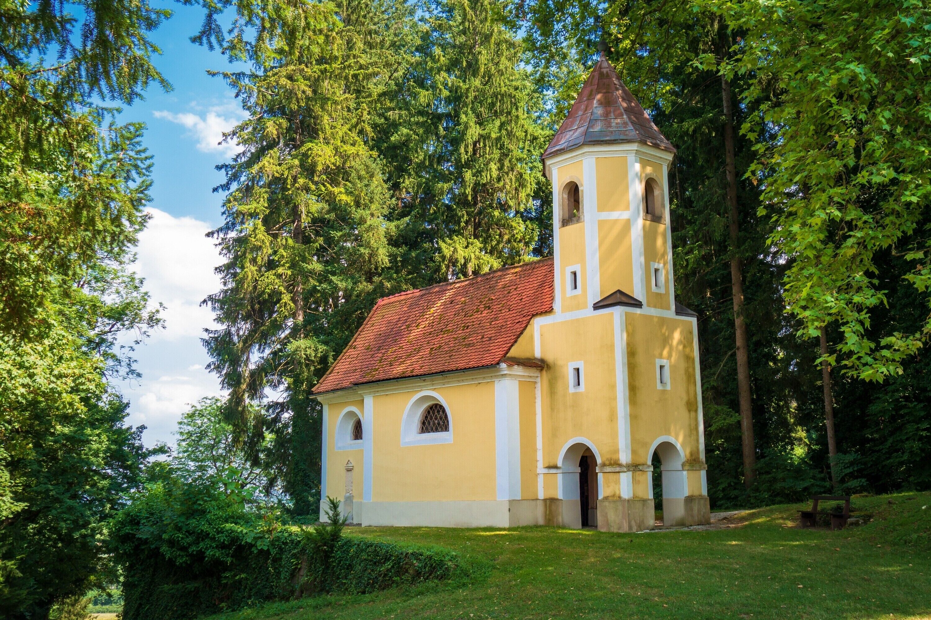 A church with a bell tower, surrounded by trees and greenery.