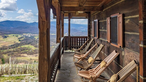 Eine hölzerne Veranda mit Holzstühlen und Blick auf eine gebirgige Landschaft.