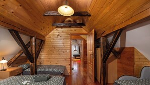Ein gemütliches Schlafzimmer im Dachgeschoss mit Holzbalken, zwei Betten mit gemusterten Betttextilien, einem Nachttisch mit Lampe sowie einem Tablett mit Tassen und einer Blume.
