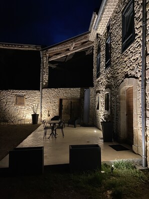 A stone building with a covered patio area, outdoor seating, and a potted plant. - Le Gite Des Rousses Charmant Corps de Ferme en Pierre Datant de 1769 (Montels)