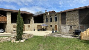 Ein Steinhhaus mit überdachter Terrasse, ein Auto davor und ein Grill.