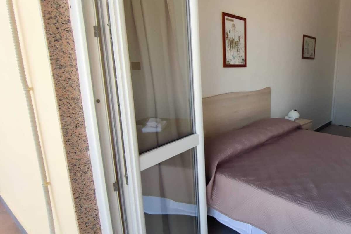 Quarto com cama, mesa de cabeceira, janela e porta.