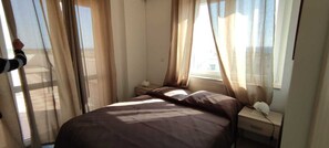 A bedroom with a bed, a nightstand, a lamp, and sheer curtains. - Volcano Home Room Resort (Alliste)