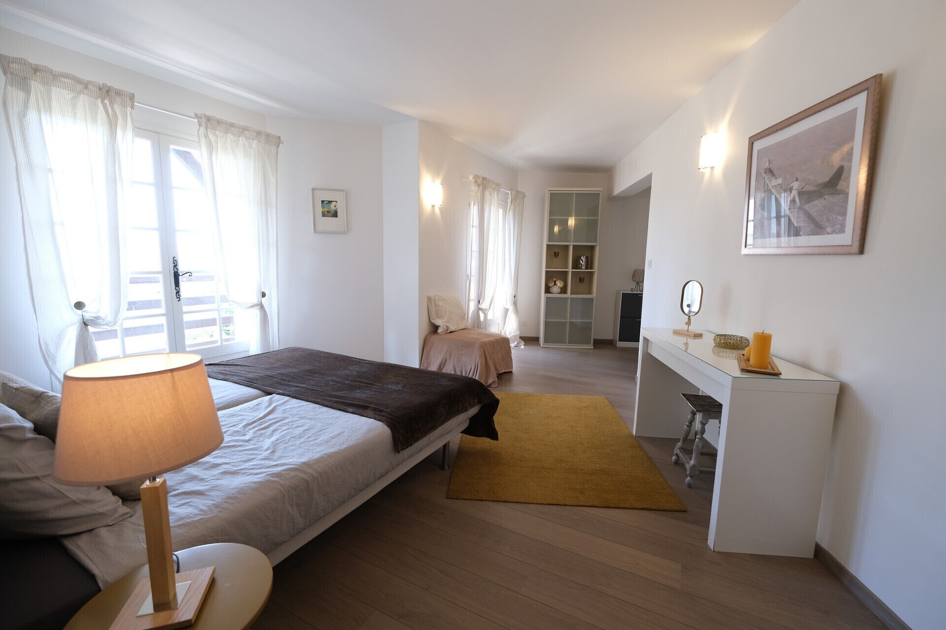 A bedroom with a bed, bedside table, lamp, and a desk with a mirror and candle.