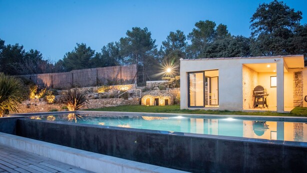 A modern outdoor pool area with a stone wall, a wooden deck, and a building with a glass door. - Holiday rental with pool SAINT CHAMAS LS7-440. (Saint-Chamas)