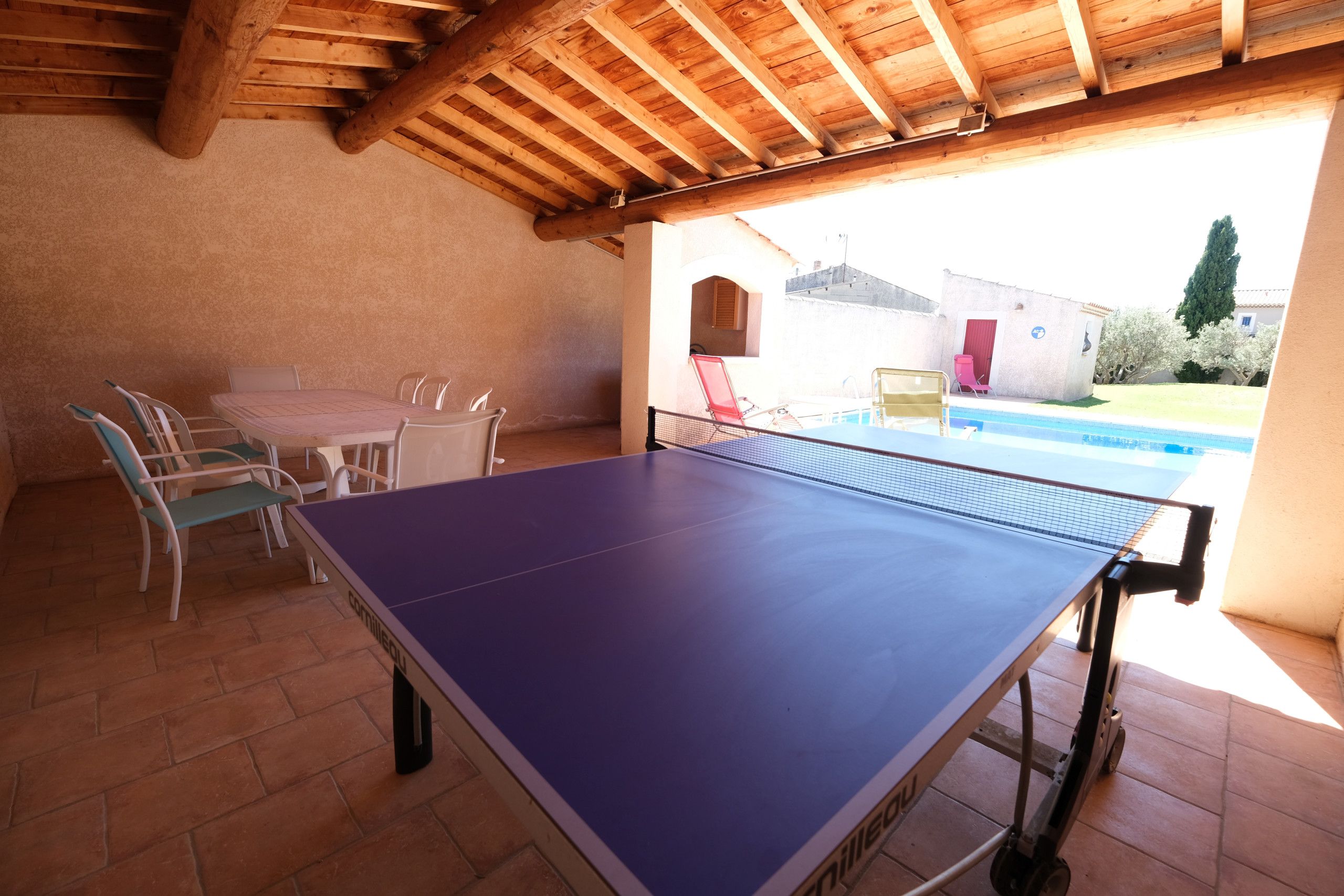 An indoor ping pong table with chairs, a small pool, and a patio area with a wooden ceiling.