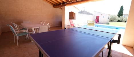 An indoor ping pong table with chairs, a small pool, and a patio area with a wooden ceiling.