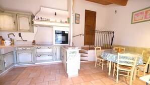 Una cocina con armarios blancos, horno empotrado y comedor con mesa y sillas.