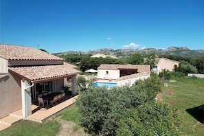 A residential area with a swimming pool, a patio with outdoor furniture, and a view of mountains in the background.