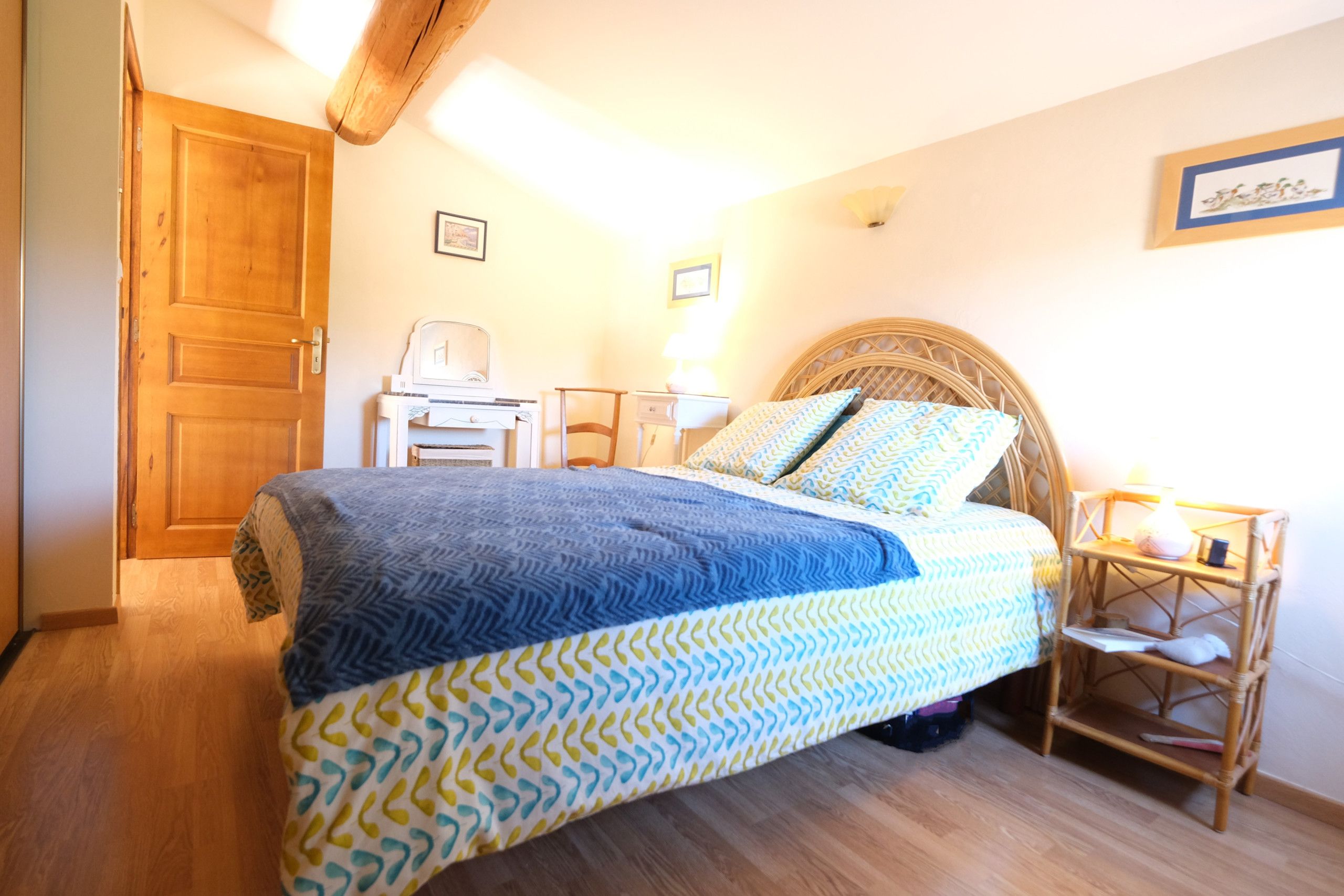 Ein Schlafzimmer mit Bett, Holztür, Nachttisch, Lampe und einem gerahmten Bild an der Wand.