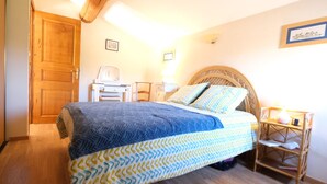 Un dormitorio con cama, puerta de madera, mesita de noche, lámpara y un cuadro enmarcado en la pared.