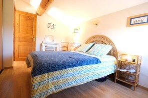A bedroom with a bed, wooden door, bedside table, lamp, and a framed picture on the wall.