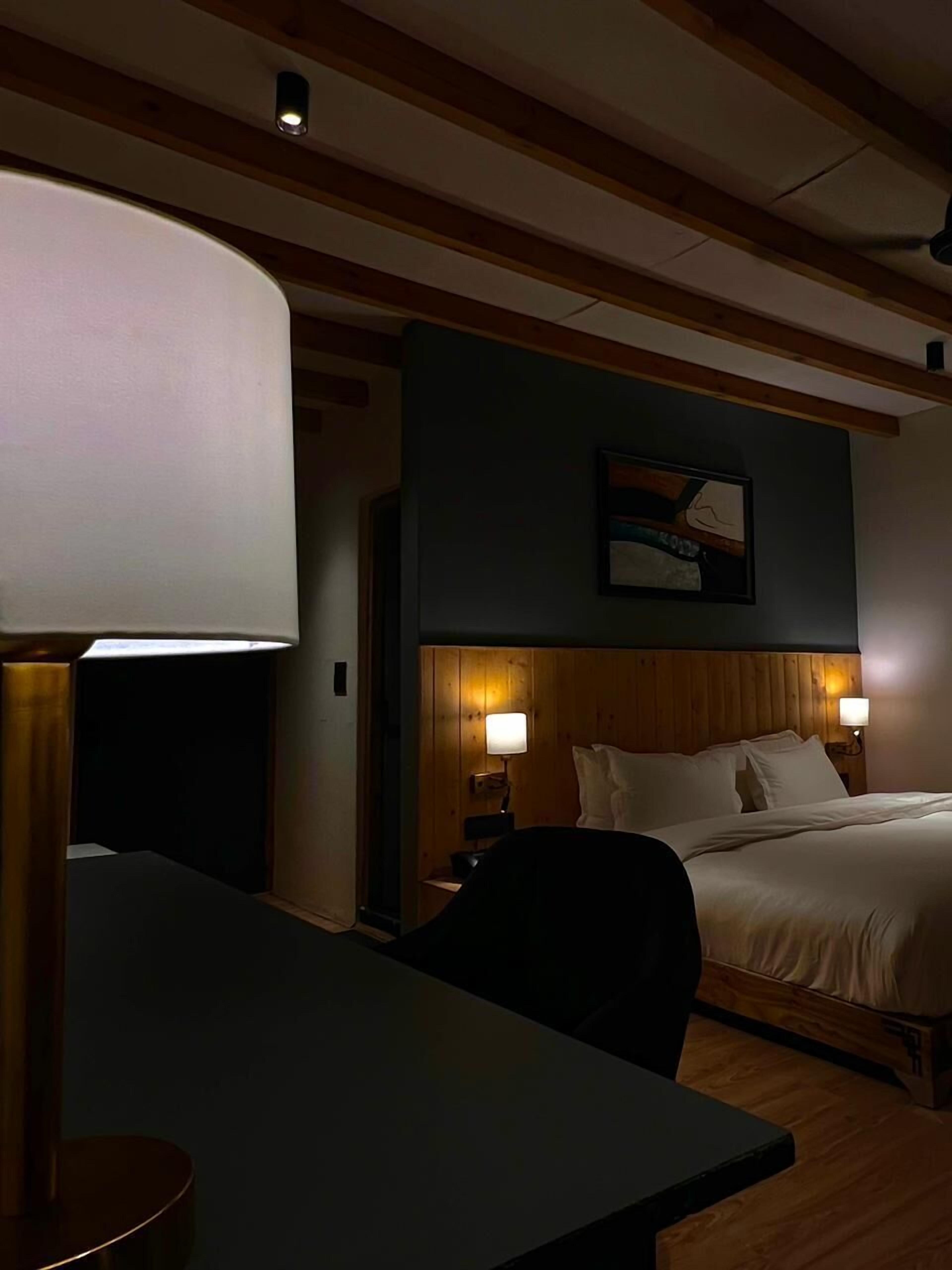 A hotel room with a bed, bedside lamps, a desk, and a wall-mounted painting.