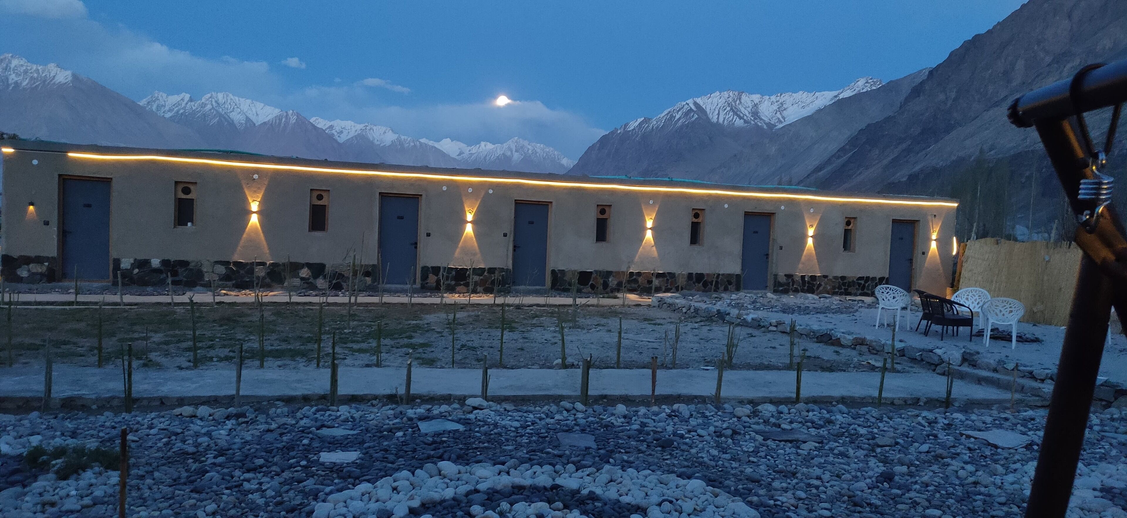 A building with multiple doors and windows, surrounded by a rocky landscape and snow-covered mountains.