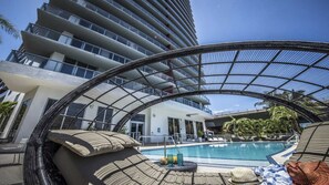 A modern hotel with a rooftop pool, lounge chairs, and a glass-enclosed terrace. - Amazing Pool|Apartment with Balcony|Near Beach (Hallandale Beach)