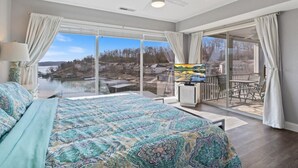 Ein Schlafzimmer mit einem großen Bett, einem Fernseher und einem Balkon mit Blick auf einen See und Gebäude.