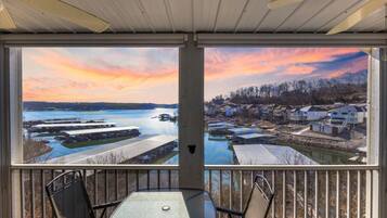 Un espacio exterior cubierto con mesa y sillas, con vista a un muelle y casas junto al agua.