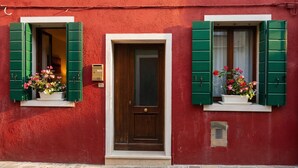 Un edificio rosso con una porta in legno e due finestre con persiane verdi.