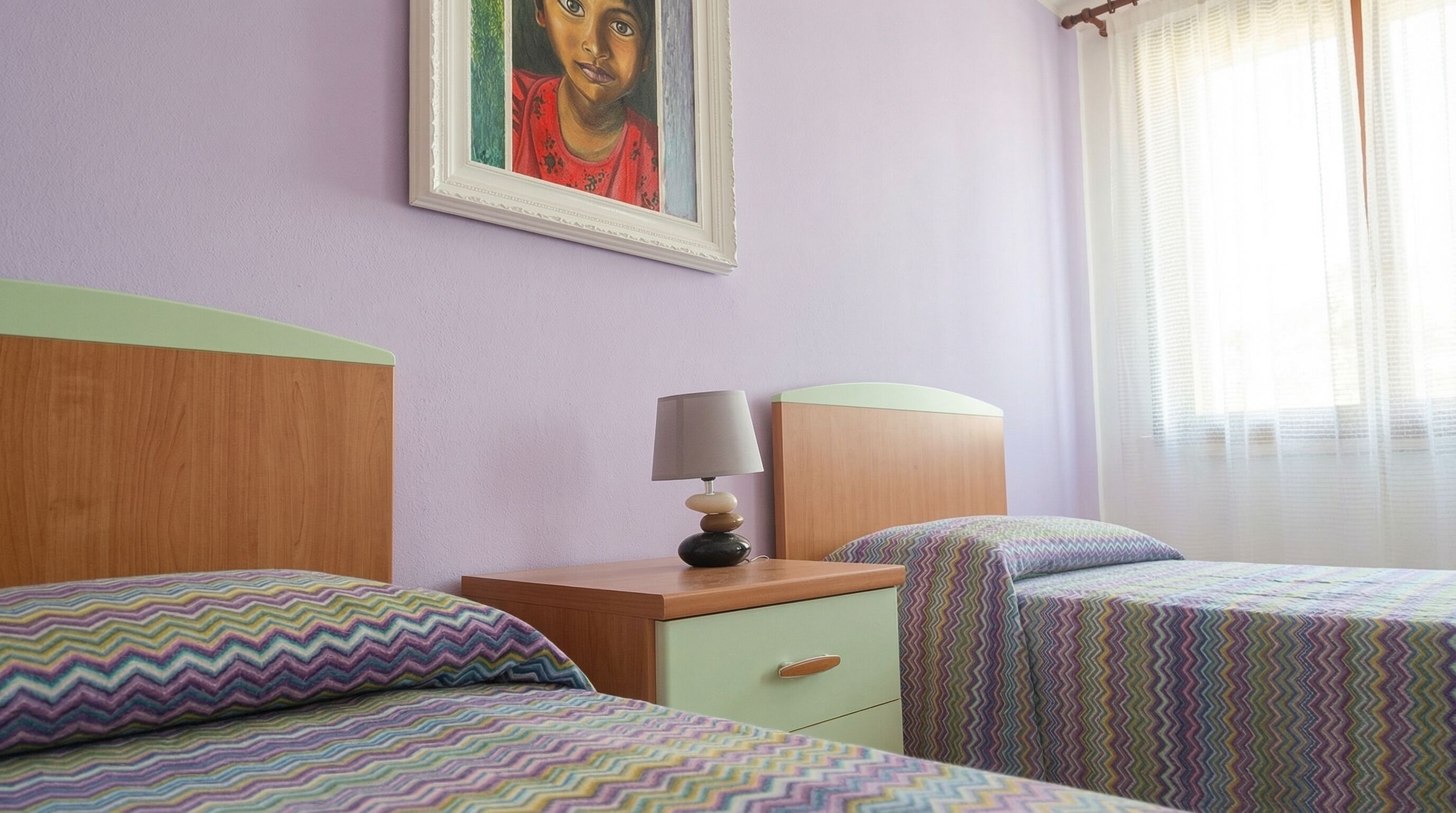 A room with two beds, a nightstand, a lamp, and a painting on the wall.