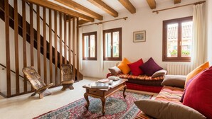Un accogliente soggiorno con una scala in legno, un divano con cuscini colorati, un tavolino da caffè e un tappeto decorato.