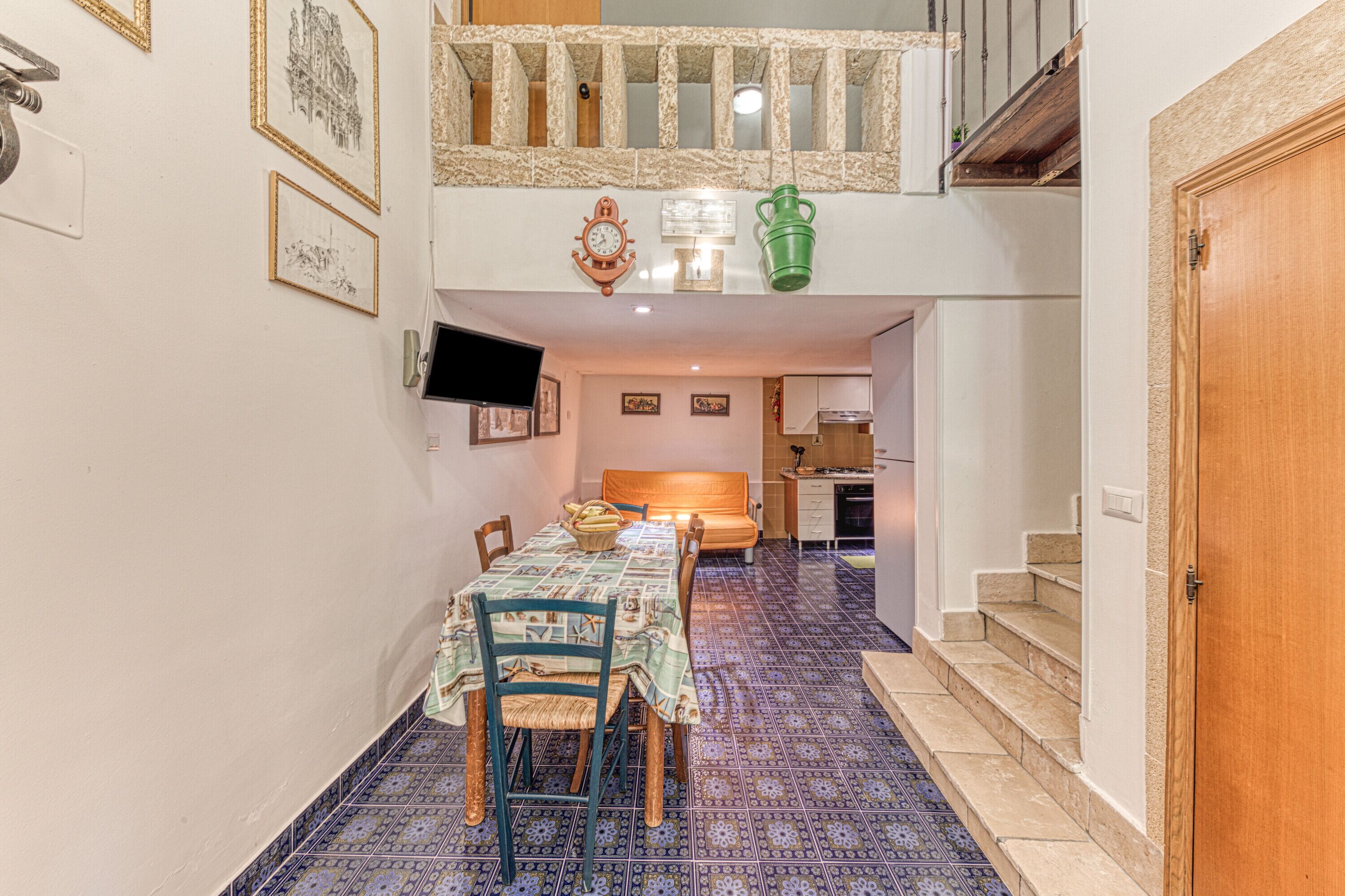 Un comedor con una mesa lista para cuatro, una cocina al fondo y una escalera que sube a un nivel superior.