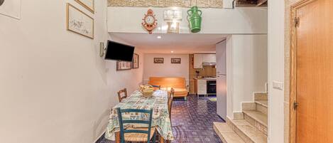 Un comedor con una mesa lista para cuatro, una cocina al fondo y una escalera que sube a un nivel superior.
