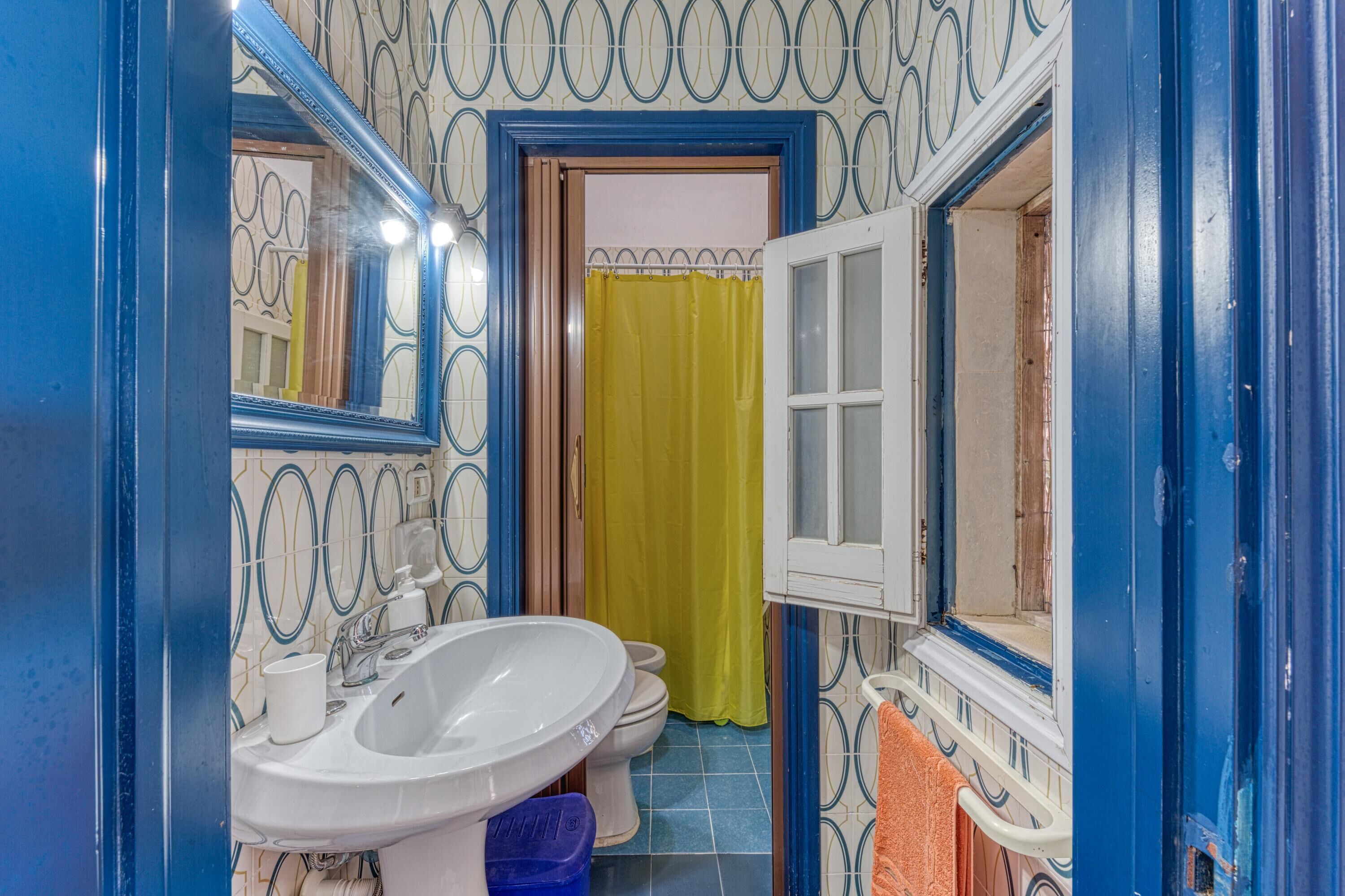 A bathroom with a white sink, a mirror, a yellow shower curtain, and a blue door.