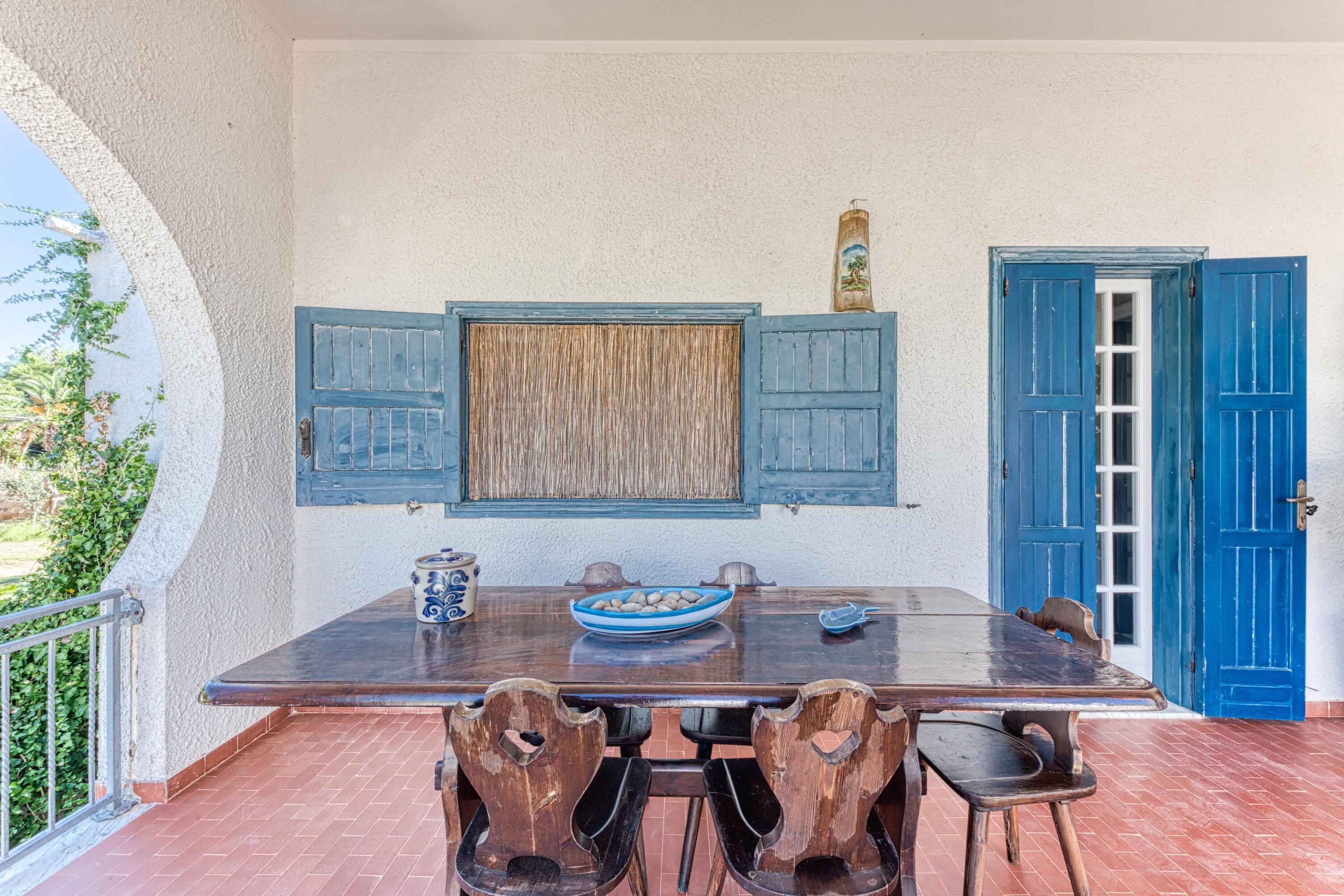 A dining area with a wooden table, blue doors, and a view of greenery.