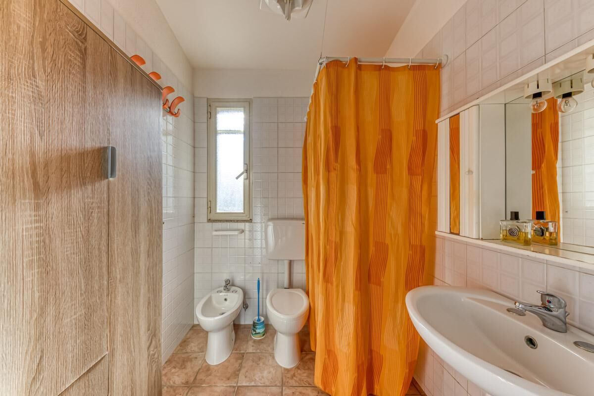 A bathroom with a wooden door, two bidets, a sink, and an orange shower curtain.