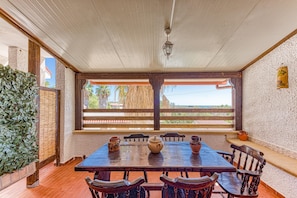 A wooden dining table with chairs, a hanging lantern, and a view of palm trees through a window. - A Casa diAmici (Salve)