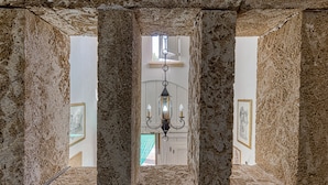 Un couloir en pierre, orné d’un lustre et de tableaux encadrés accrochés aux murs.
