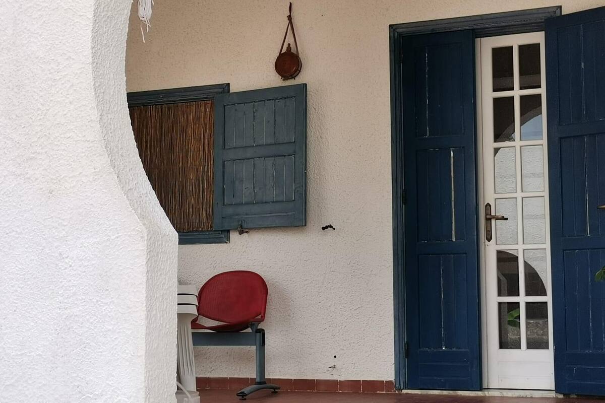 Een kamer met een rode stoel, een blauwe deur en een raam met blauwe luiken.