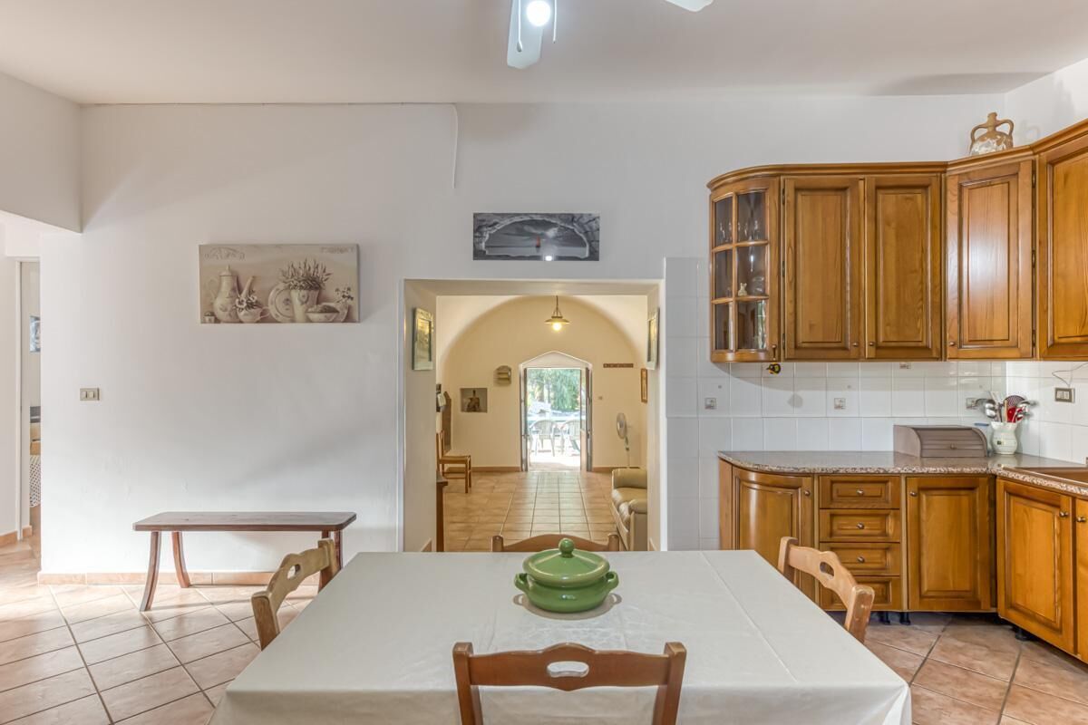 A dining area with a table, chairs, a green pot, wooden cabinets, and a hallway leading to a living area.