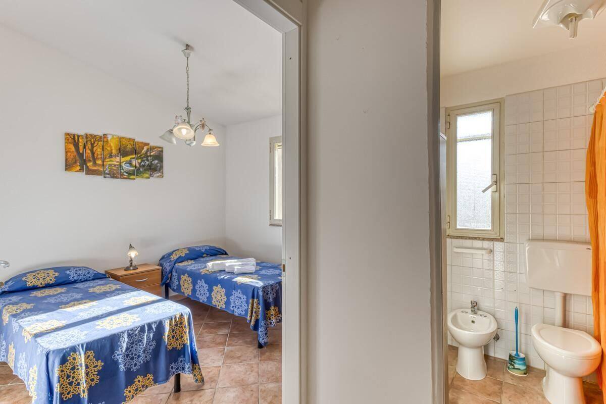 Een kamer met twee bedden, een badkamer met toilet, bidet en wastafel, en een plafondlamp.