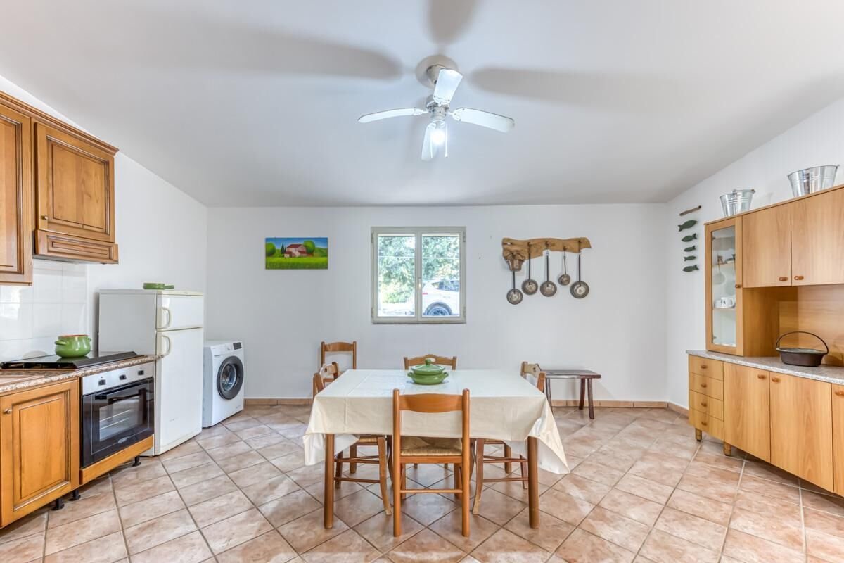 A kitchen with wooden cabinets, a dining table, chairs, a ceiling fan, a washing machine, and a refrigerator.