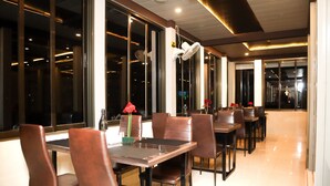 Un restaurant au décor moderne, avec une grande table à manger entourée de chaises, de grandes fenêtres et un ventilateur de plafond.