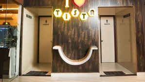 Un hall d'accueil d'hôtel avec un panneau néon sur lequel on peut lire « I ♥ TOSTO » et deux portes indiquant « TOILETTES DAMES » et « TOILETTES HOMMES ».