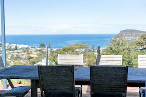 A table with chairs facing a scenic view of the ocean and a hilly landscape.