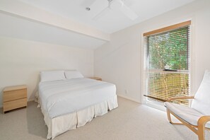 A bedroom with a bed, a nightstand, a chair, a window with blinds, and a ceiling fan.