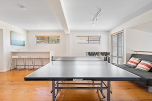 Uma mesa de ping pong em um quarto com piso de madeira, um sofá e uma área de jantar com cadeiras.