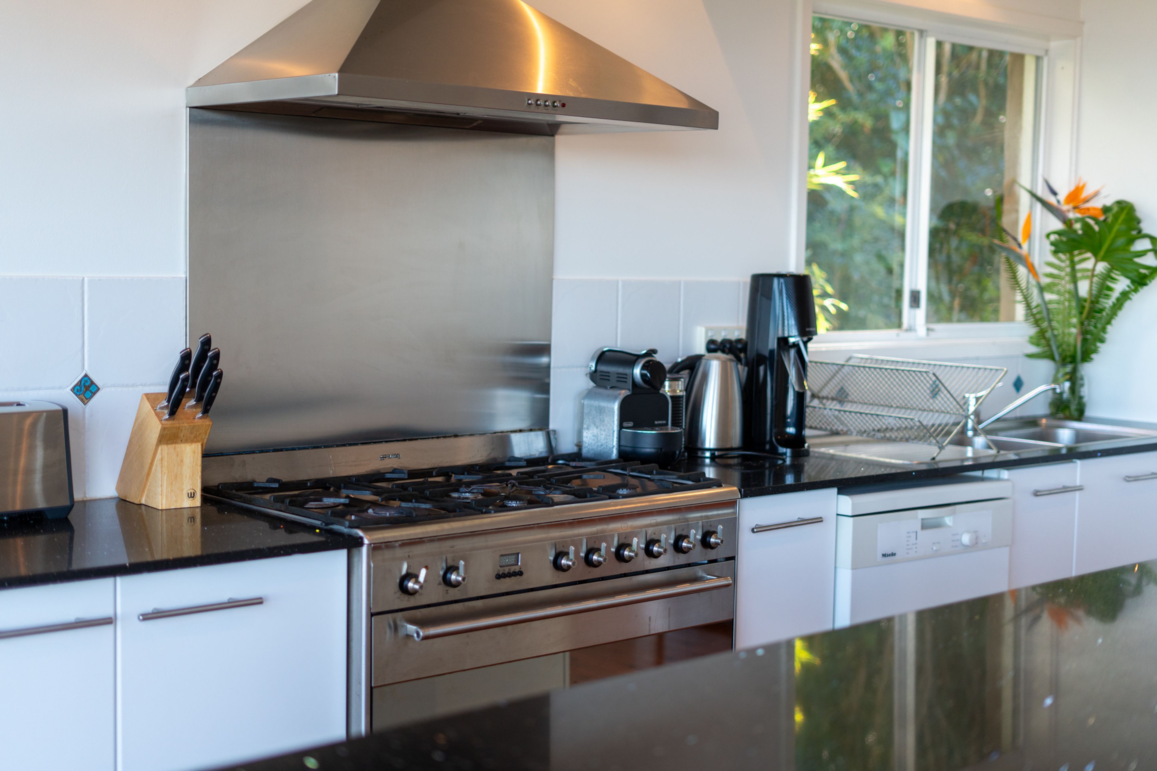 Cozinha moderna com fogão de aço inoxidável, cafeteira e janela com vista para área verde.