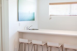 A kitchen with a stainless steel sink, a window with blinds, and a bar area with four bar stools.
