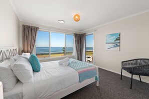 A hotel room with a bed, a chair, a painting, and a view of the beach.