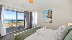 Une chambre d’hôtel avec un lit, un tableau représentant une scène de plage, une vue sur la mer par une porte coulissante et un balcon donnant sur la mer.