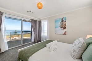 Une chambre d’hôtel avec un lit, un tableau représentant une scène de plage, une vue sur la mer par une porte coulissante et un balcon donnant sur la mer.